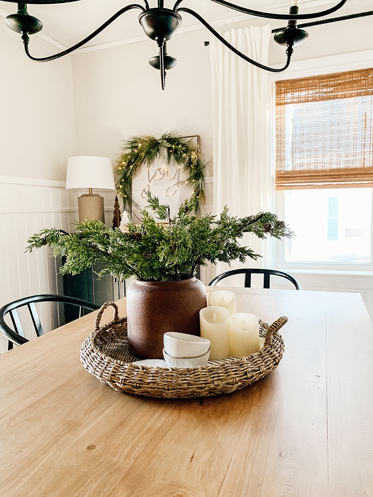 Christmas Dining Room featuring a small lit christmas tree, large black chandelier, wreath lit up with the words joy, wood table and black dining chairs.