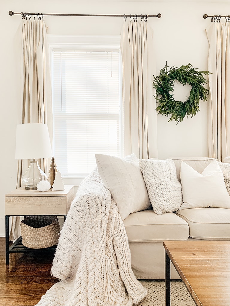 Simple neutral Christmas living room with slip cover couches a lit artificial tree in the corner and a cedar wreath on the wall.