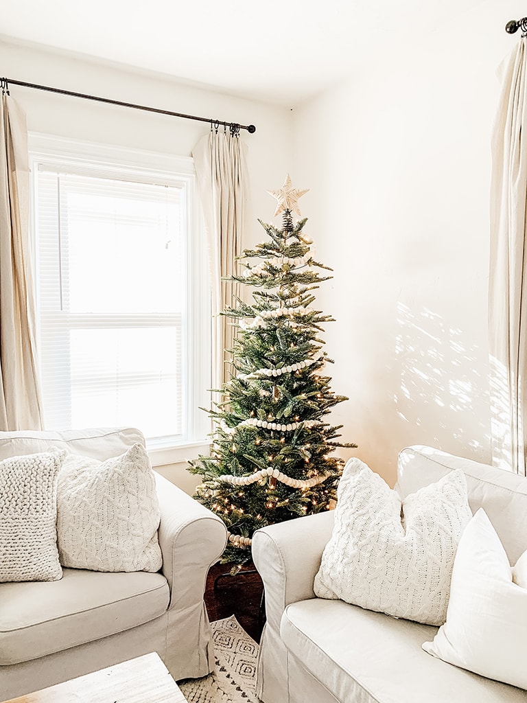 Simple neutral Christmas living room with slip cover couches a lit artificial tree in the corner and a cedar wreath on the wall.