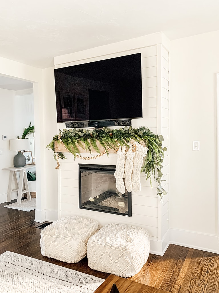 Shiplap fireplace decorated for christmas with pine, cedar and eucalyptus garland as wella large wood bead garland. Featuring an electric fireplace.