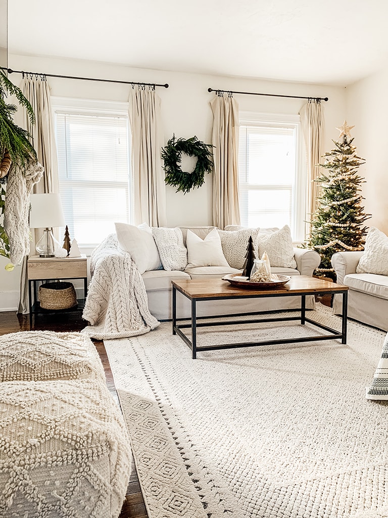 Simple neutral Christmas living room with slip cover couches a lit artificial tree in the corner and a cedar wreath on the wall.